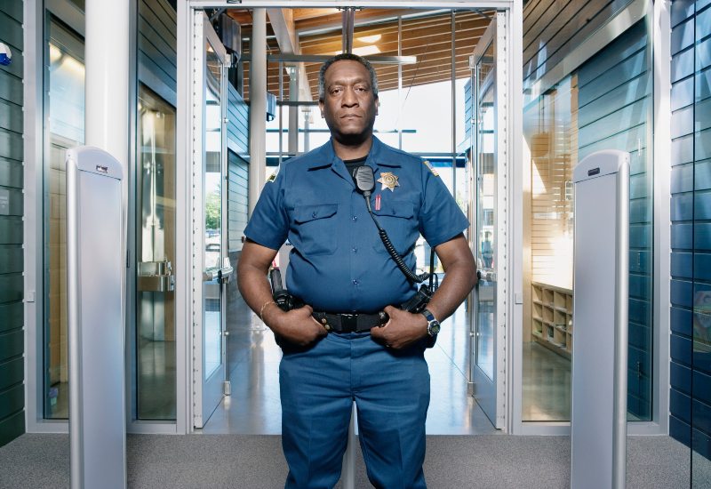A bank security guard in a blue uniform stands in front of a security door in San Jose, CA.